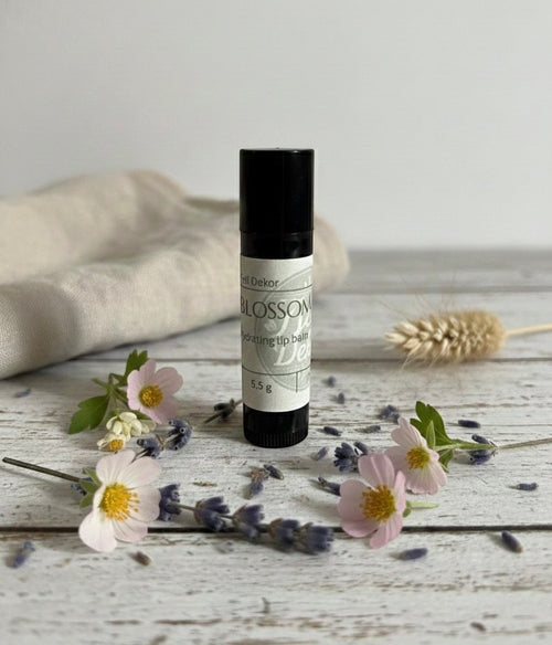 Fjell Dekor Blossom Kiss natural hydrating lip balm in a black tube surrounded by small pink flowers and lavender.