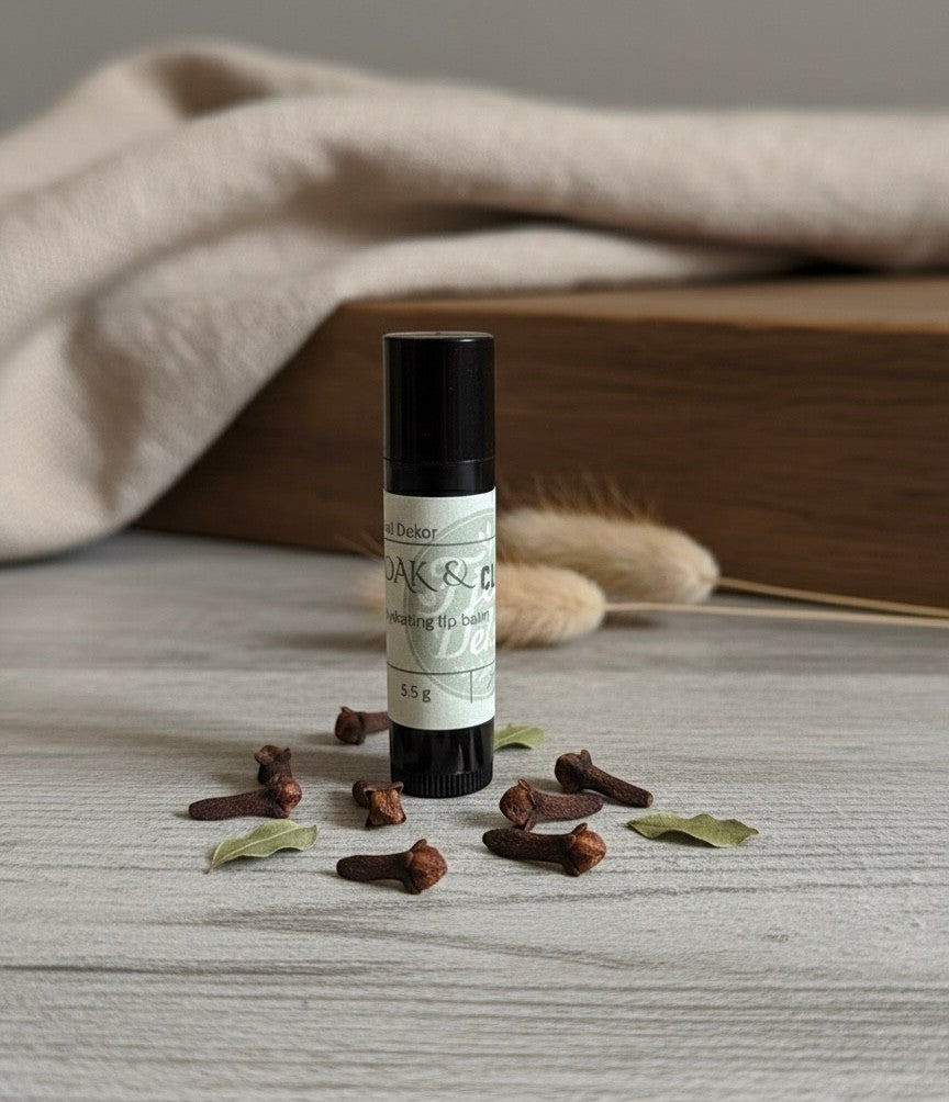 Fjell Dekor Oak and Clove natural lip balm in a black tube surrounded by whole cloves on a rustic wooden surface.