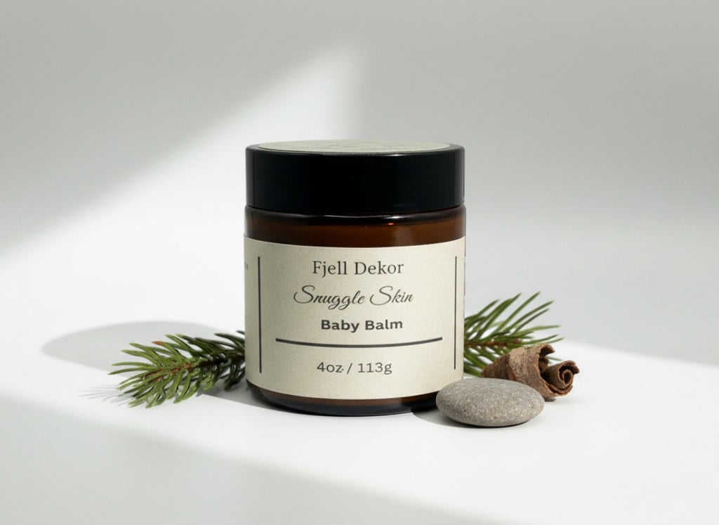 Fjell Dekor Snuggle Skin Baby Balm in a 4oz amber glass jar with a black lid, styled with pine needles and a stone.