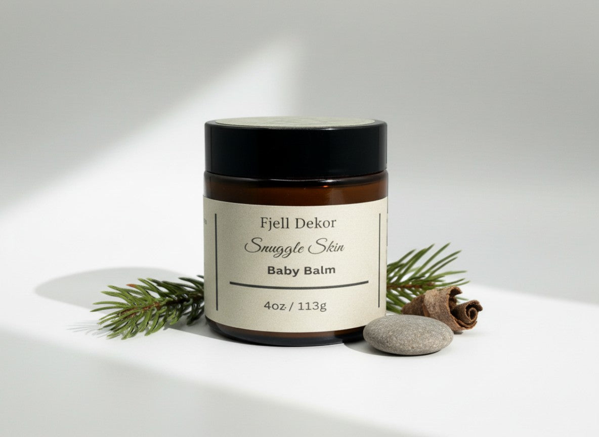Fjell Dekor Snuggle Skin Baby Balm in a 4oz amber glass jar with a black lid, styled with pine needles and a stone.